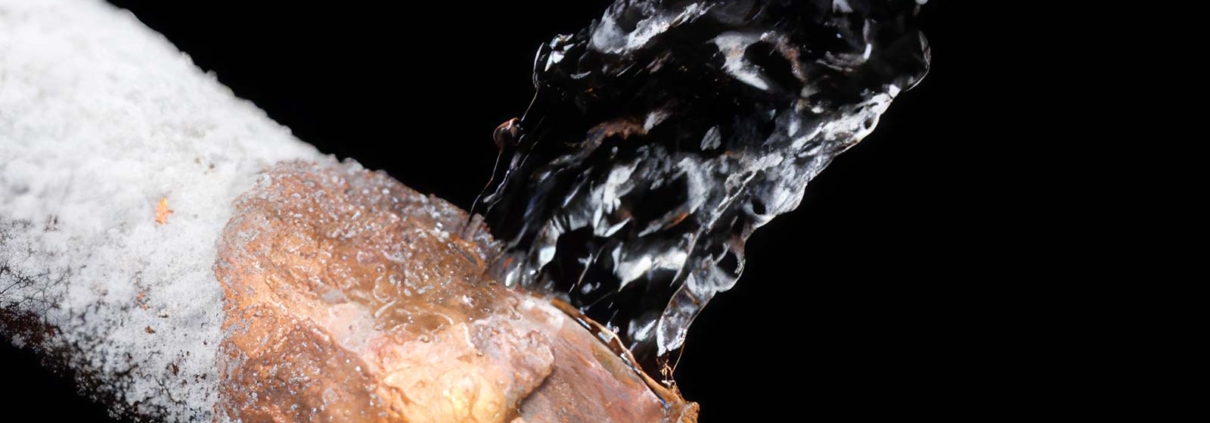 Close-up of a frozen copper pipe bursting and spraying water due to ice buildup.