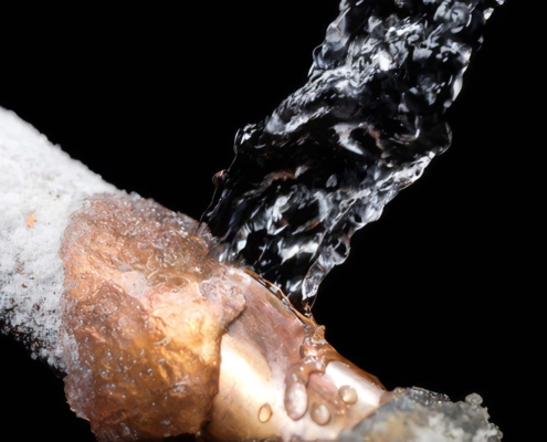 Close-up of a frozen copper pipe bursting and spraying water due to ice buildup.