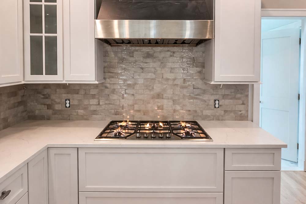Gas cooktop installation with stainless steel range hood and tile backsplash.