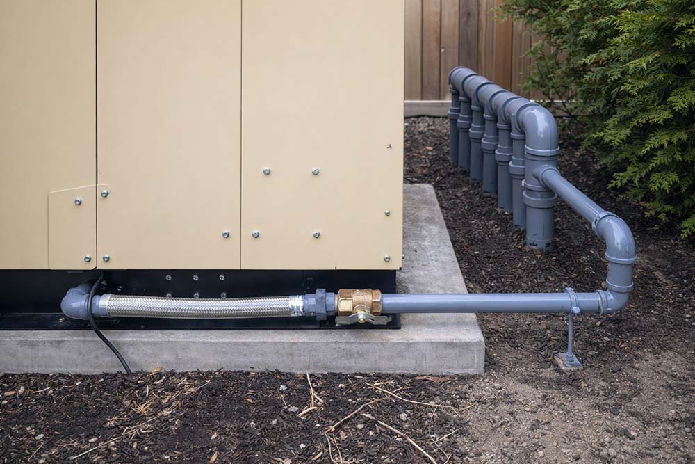 Outdoor gas piping installation with gray PVC piping, brass shutoff valve, and flexible stainless steel gas connector attached to exterior utility unit.