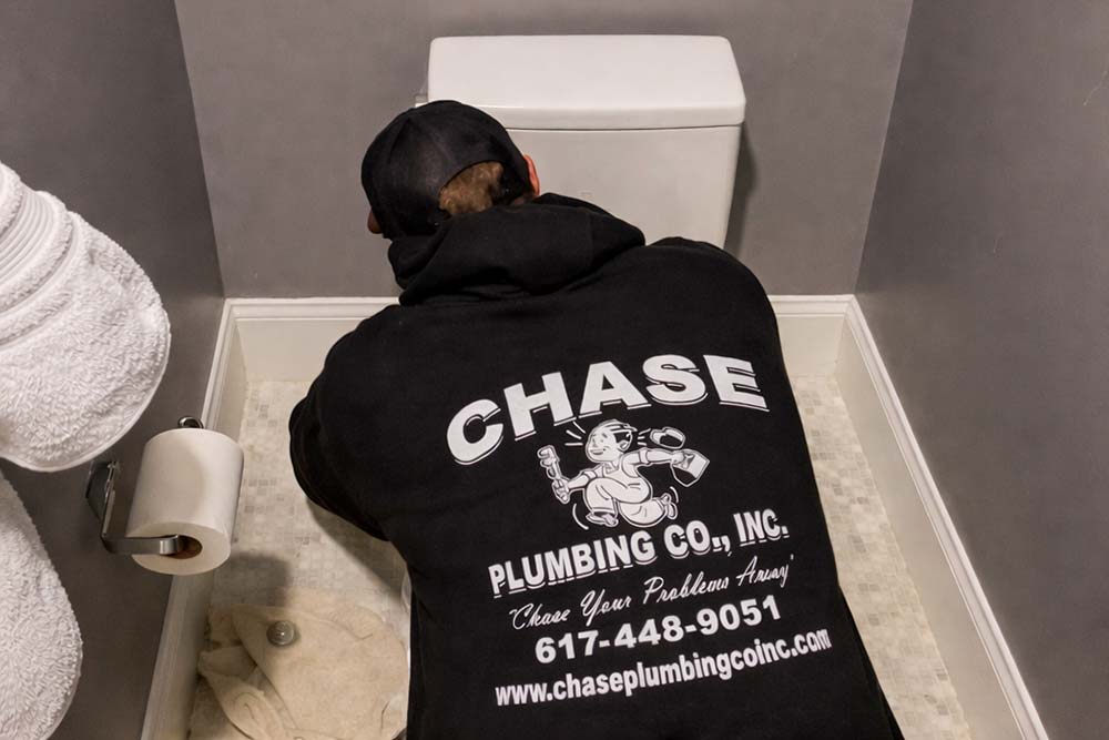 Professional plumber from Chase Plumbing Co. performing toilet repair in a residential bathroom.