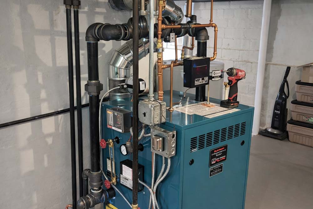 Residential steam boiler installation with copper and black pipe connections in basement.