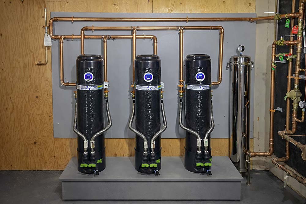 Three whole-house water filtration units installed in a basement with copper piping and stainless pre-filter system.