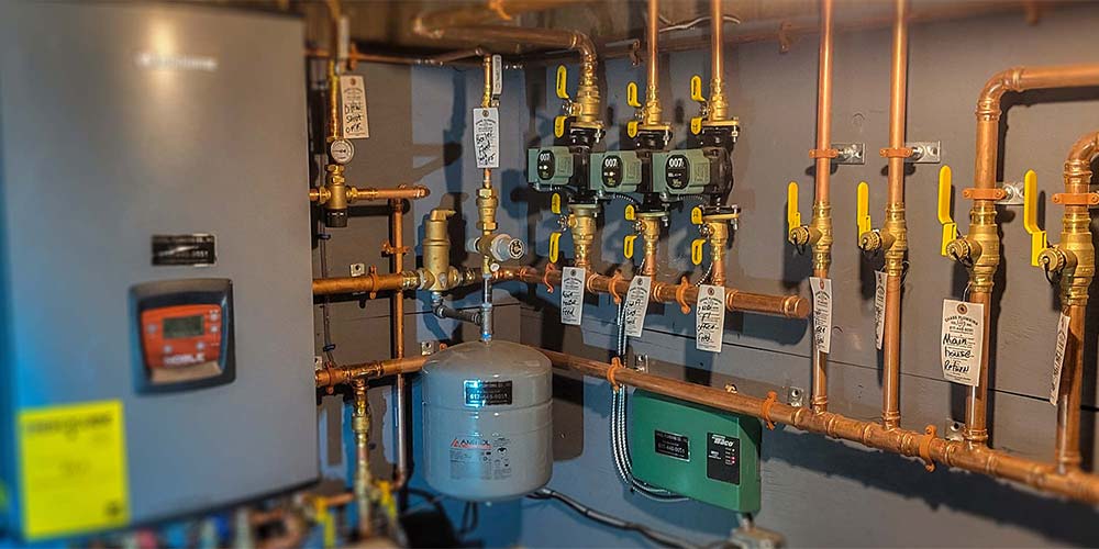 Residential boiler system with copper piping, circulation pumps, and shutoff valves installed in a mechanical room.