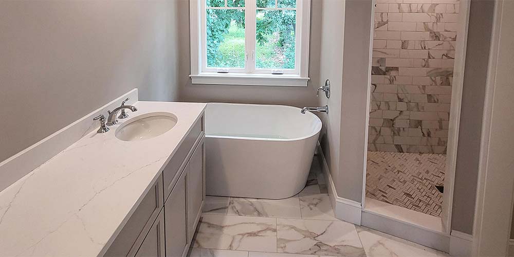Newly remodeled bathroom with vanity sink, freestanding bathtub, and tiled walk-in shower.